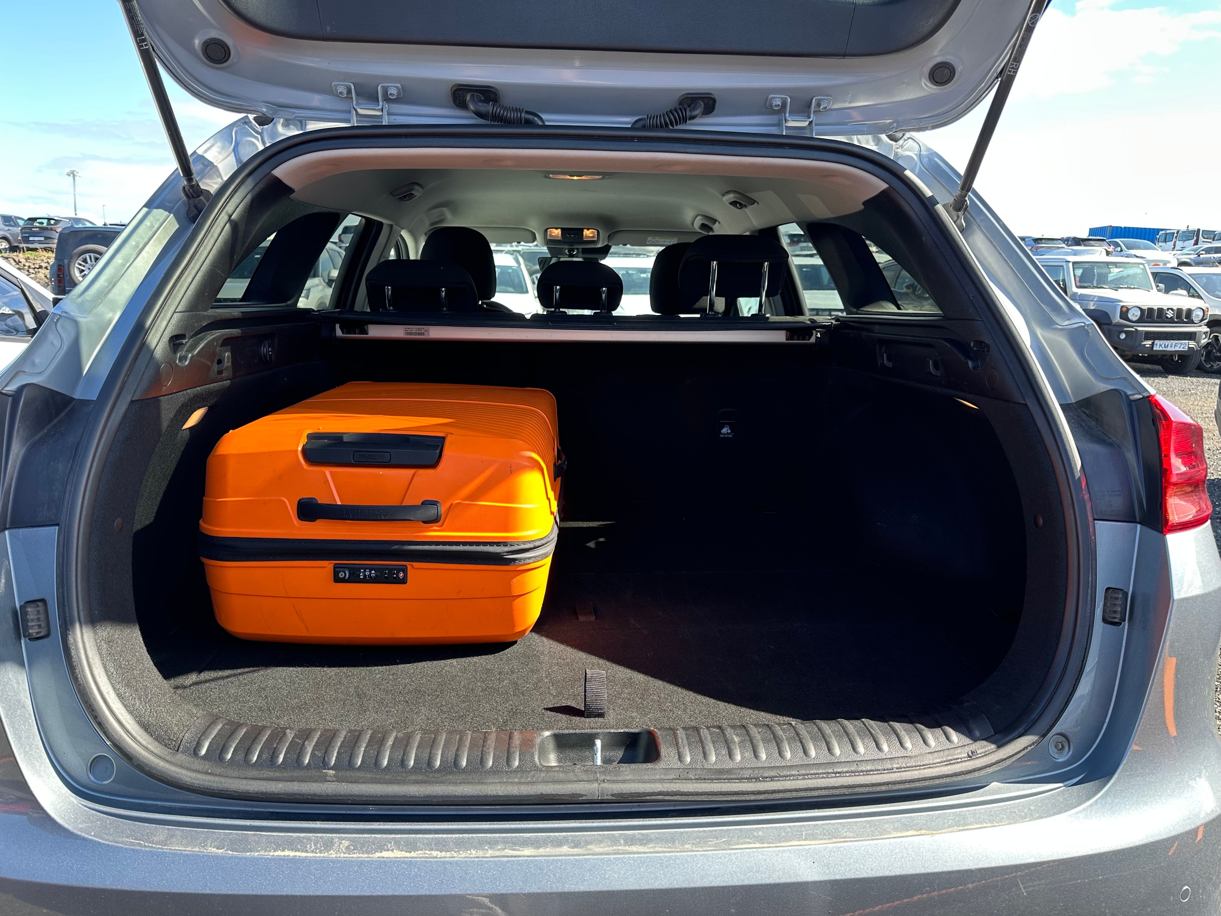 An orange suitcase in the open trunk of a grey car.