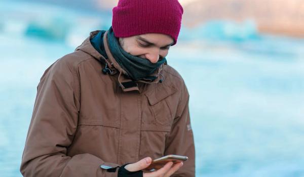 Guy-Touristenspaziergänge im Winter in Island. schaut auf sein Telefon mit geöffneter App.