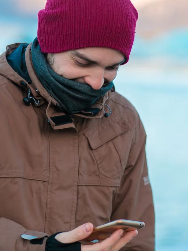 Guy-Touristenspaziergänge im Winter in Island. schaut auf sein Telefon mit geöffneter App.