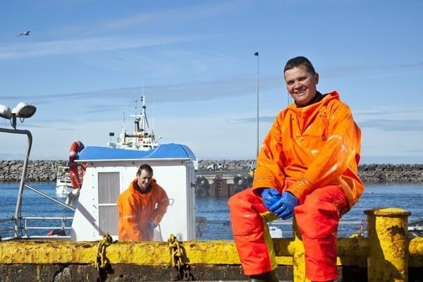 a man is sitting on a yellow dock next to a boat, Icelandic fishermen in iceland.