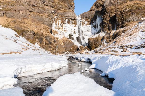 a river flowing through a snowy valley with a waterfall in the background at hvolsvollur iceland.