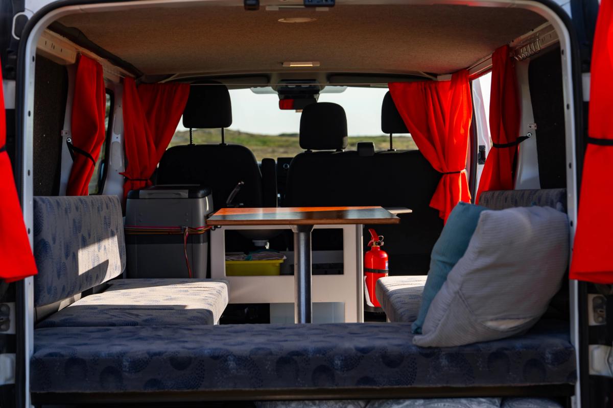 Bench seating around a central table, with a fire extinguisher and 3 front seats beyond