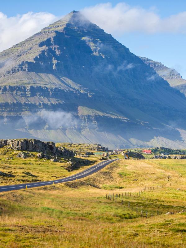 a road going through a grassy field with a mountain in the background on the artic coast way in iceland.