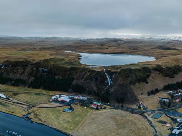 Panoramic aerial view of a plateau lake with a waterfall, a winding river, and a village, under an overcast sky.