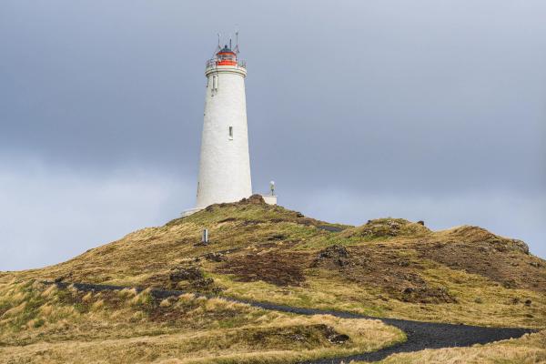 a white lighthouse is sitting on top of a grassy hill .