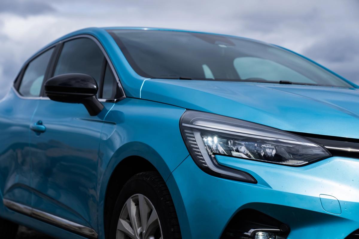 Nahaufnahme des Frontscheinwerfers und der Motorhaube eines Renault Clio vor bewölktem Himmel