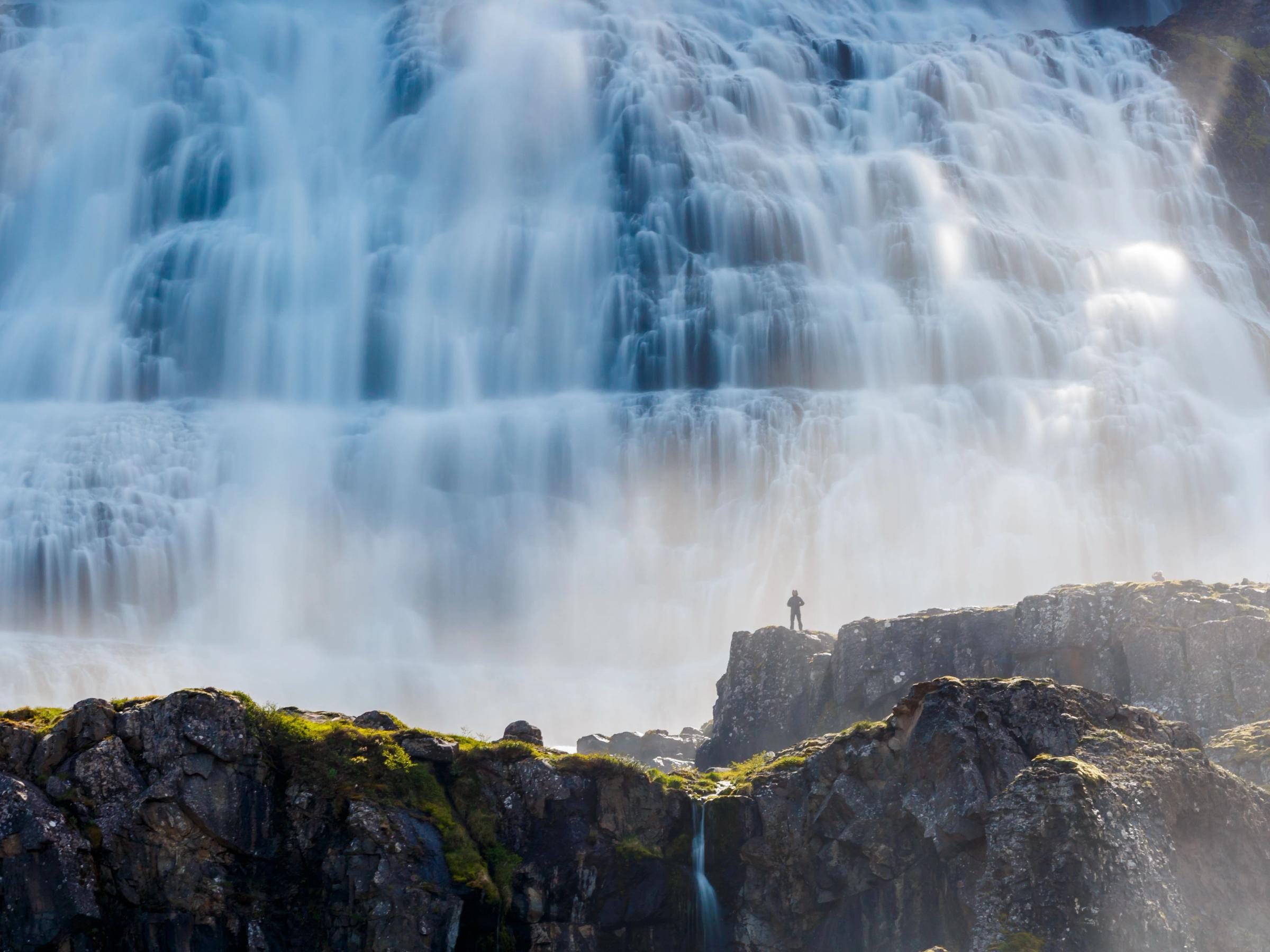 a man is standing on a rock near a waterfall .