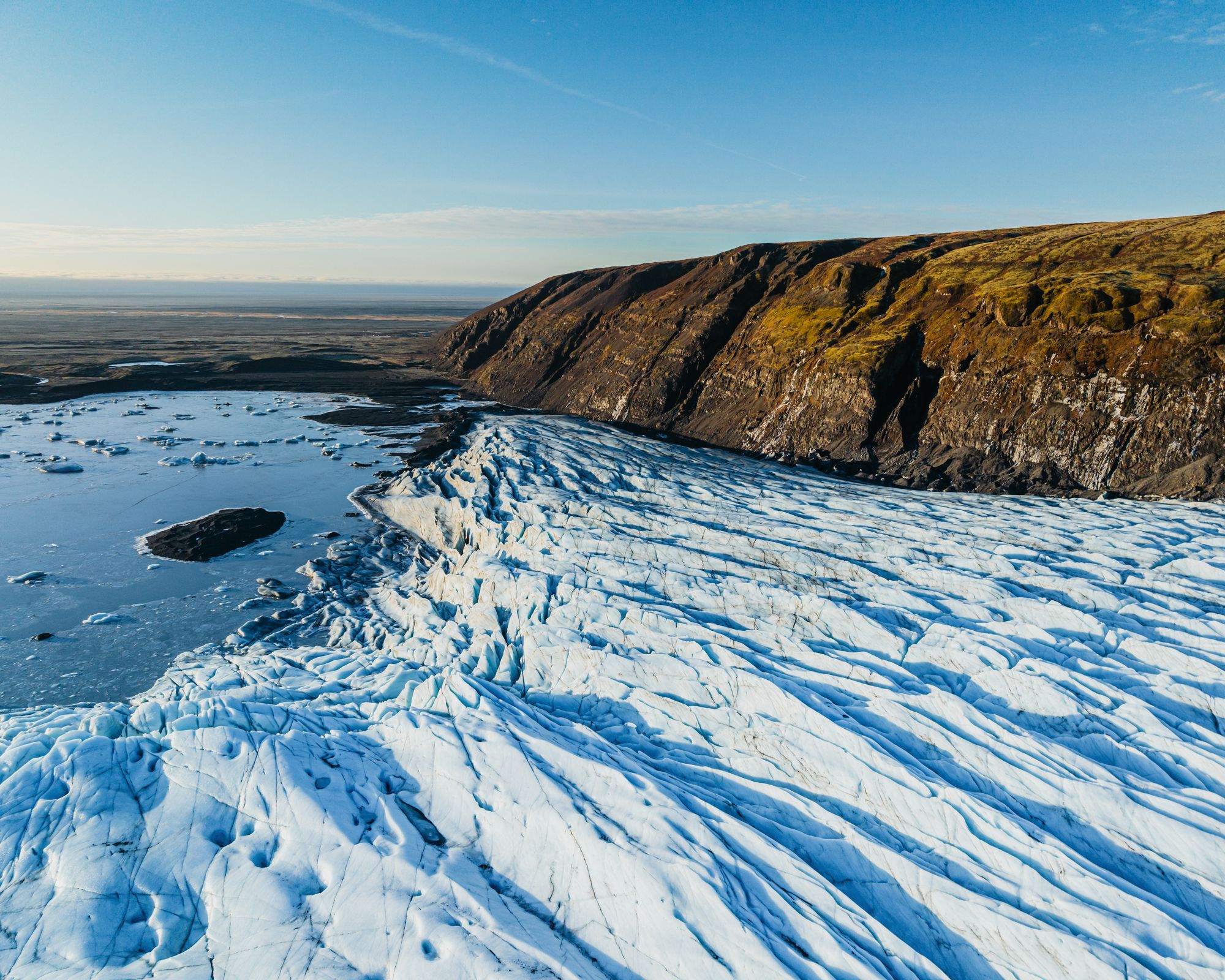 an aerial view of a glacier in iceland with a blue sky in the background at skaftafellsjökull.