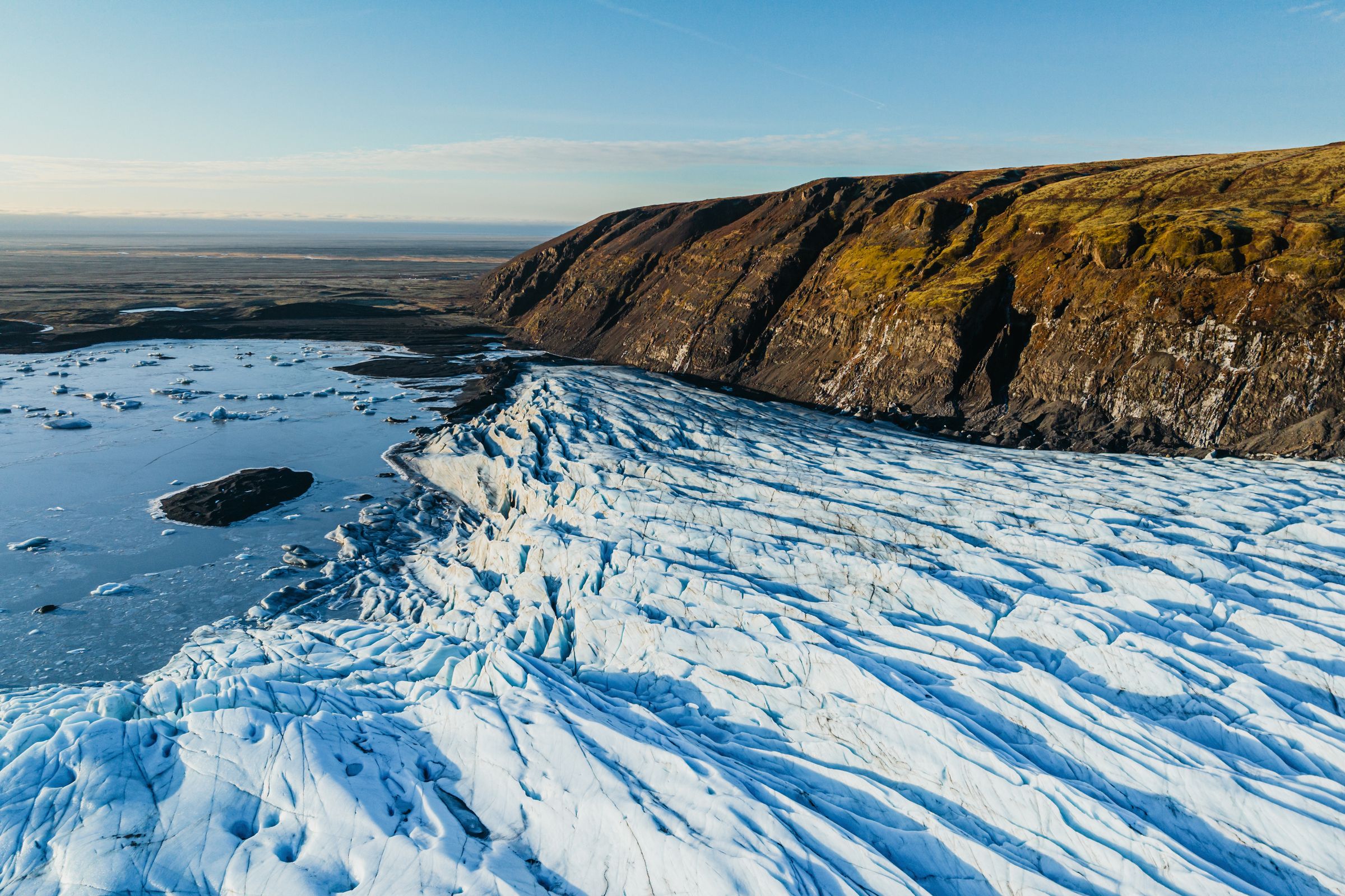 an aerial view of a glacier in iceland with a blue sky in the background at skaftafellsjökull.