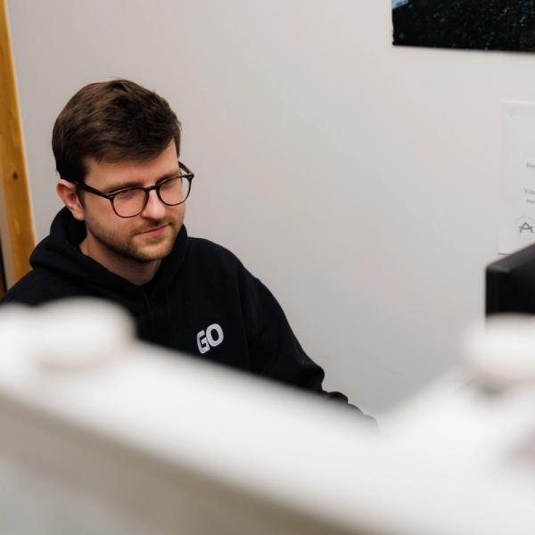 a man wearing glasses is sitting in front of a computer screen .