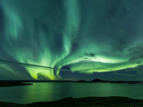 the aurora borealis is dancing in the night sky over a body of water .