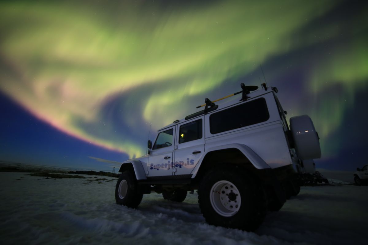 Un jeep blanco aparcado en la nieve bajo la aurora boreal.