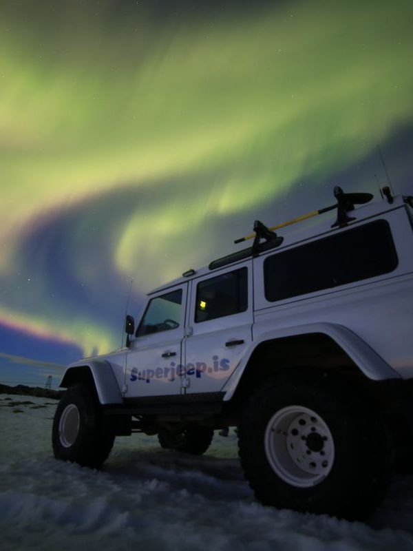 Un jeep blanco aparcado en la nieve bajo la aurora boreal.
