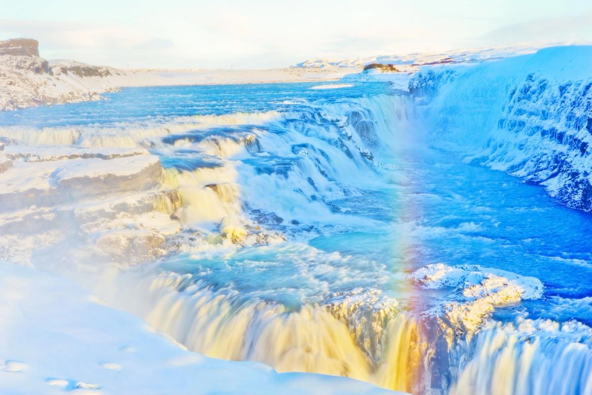 Winter waterfall cascading through a snowy landscape with a bright rainbow in the mist.