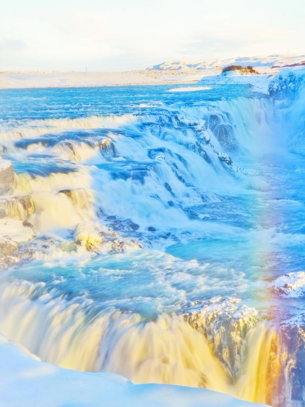 Winter waterfall cascading through a snowy landscape with a bright rainbow in the mist.