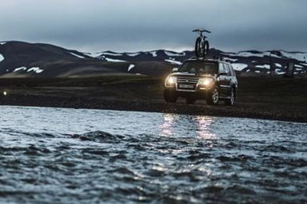 a car with a bike on top of it is driving through a river .