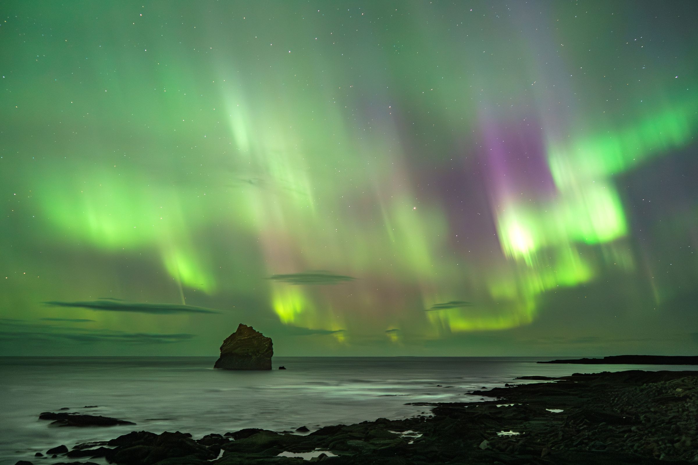 the aurora borealis is dancing in the night sky over the ocean in iceland.