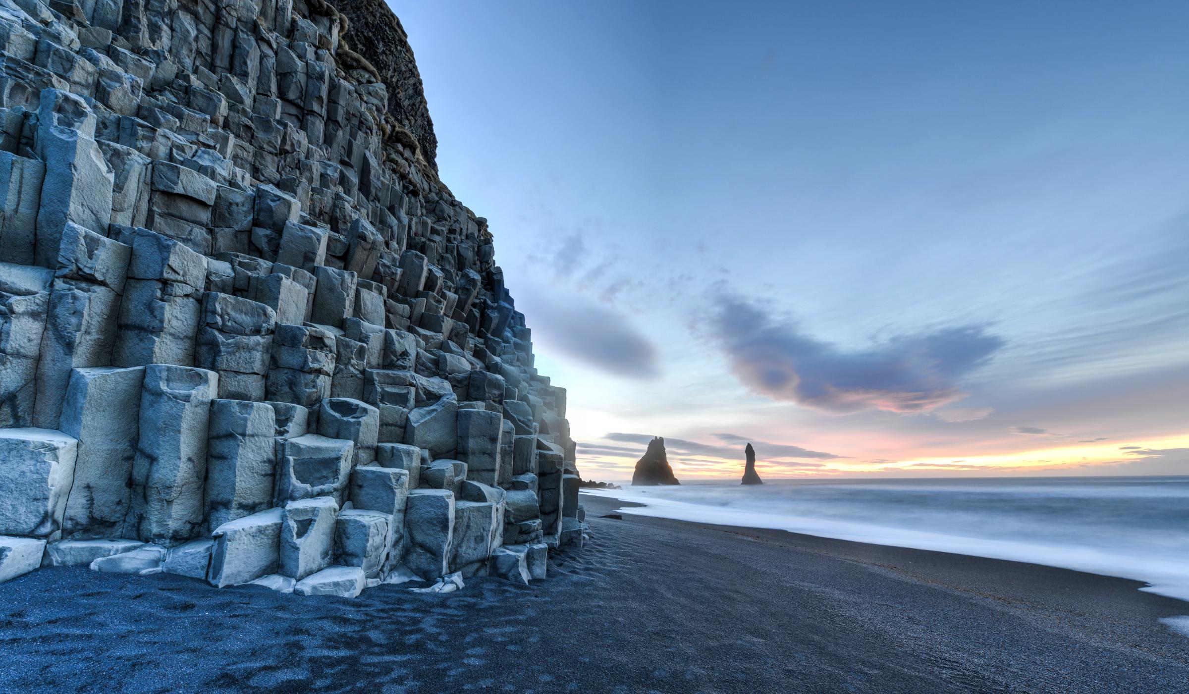 une plage de sable noir avec une grande formation rocheuse en arrière-plan à Reynisfjara en Islande.