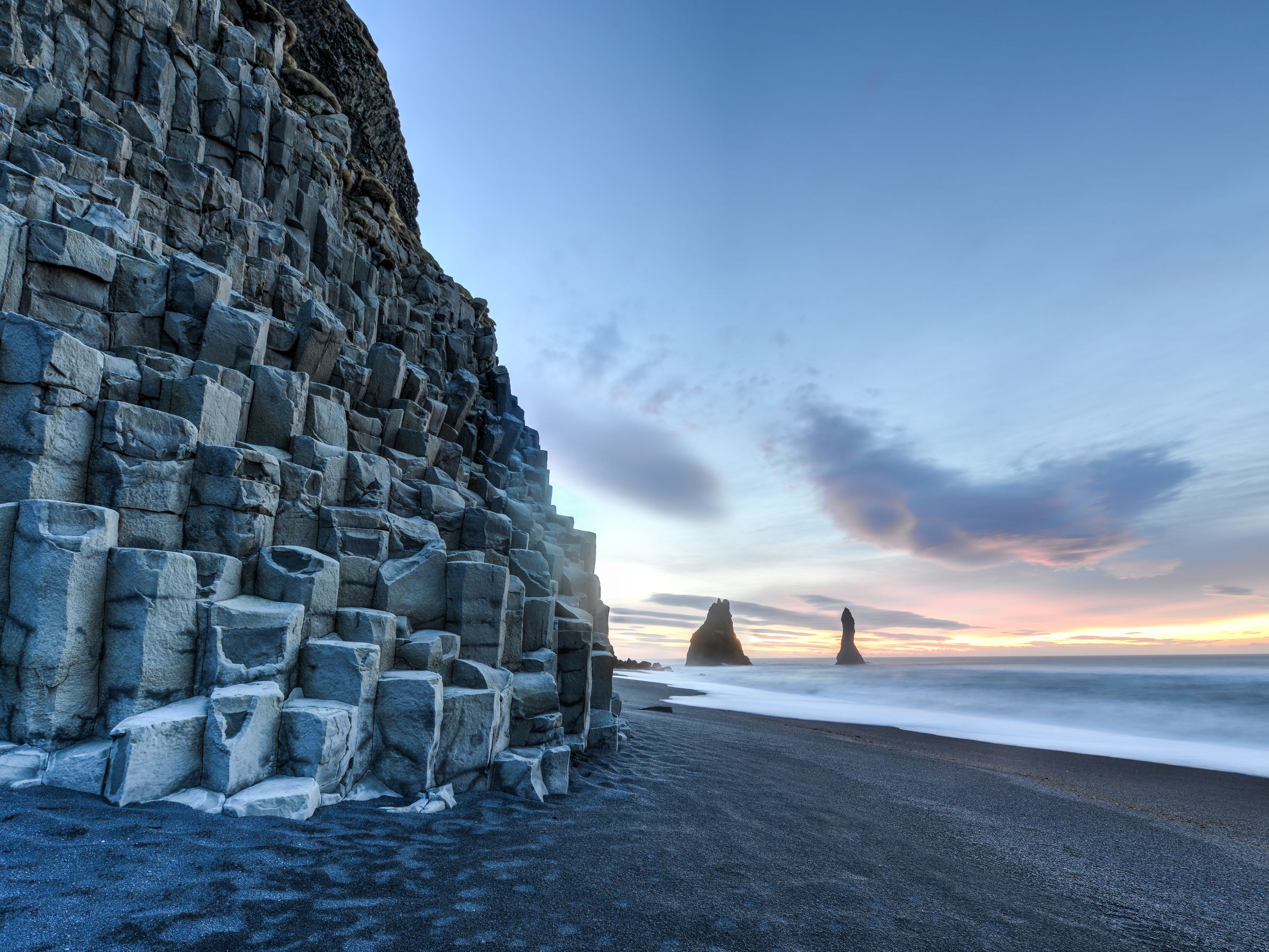 une plage de sable noir avec une grande formation rocheuse en arrière-plan à Reynisfjara en Islande.