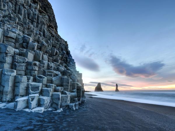 une plage de sable noir avec une grande formation rocheuse en arrière-plan à Reynisfjara en Islande.