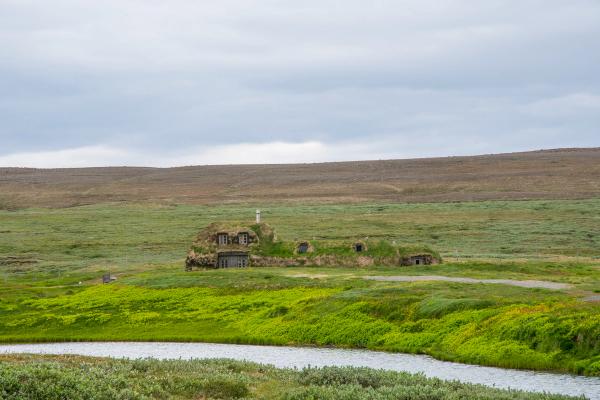 una pequeña casa está situada en medio de un campo herboso junto a un río .