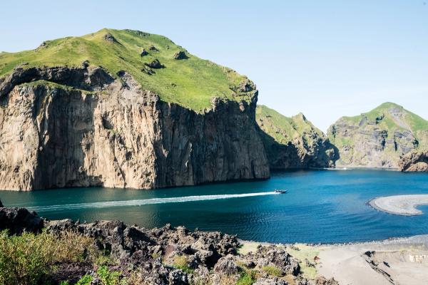 A boat leaves a wake in a calm bay surrounded by steep, green cliffs.
