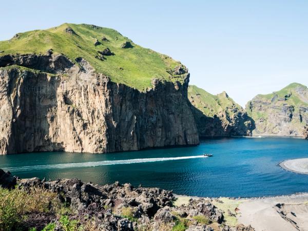 a Wake created by a small boat in the sea next to a cliff