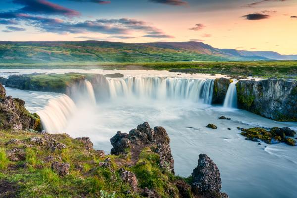 une cascade au milieu d'une rivière avec des montagnes en arrière-plan à Goðafoss en Islande.
