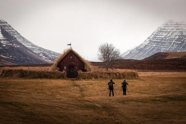 two people are standing in front of a thatched hut in a field .