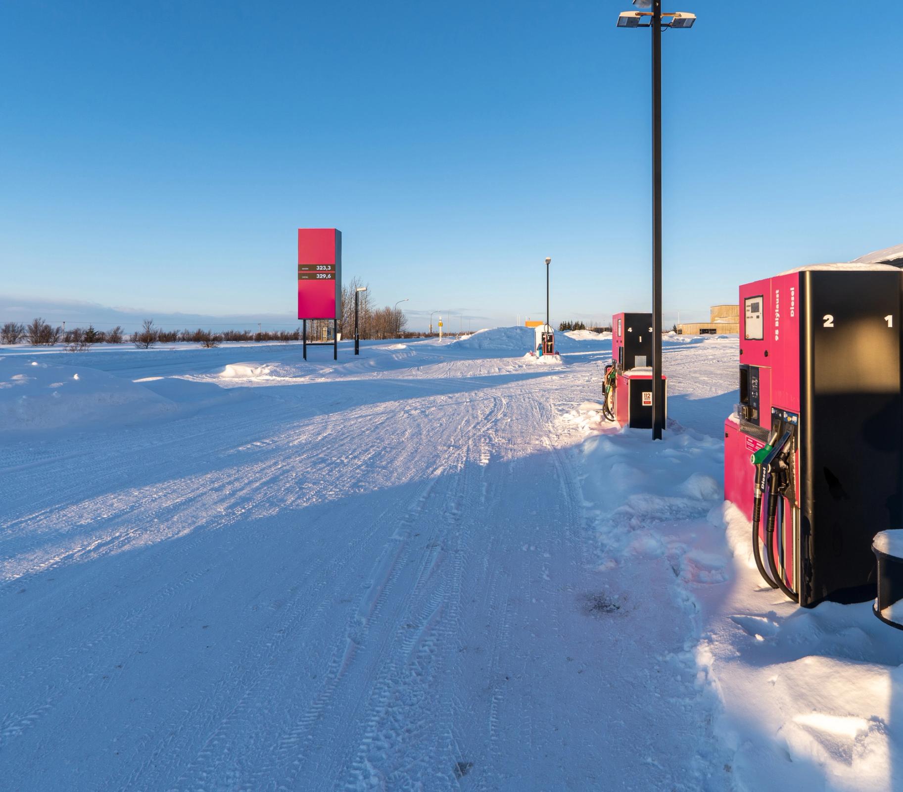 A gas station in a snowy landscape with pink pumps and a price sign under a clear blue sky.