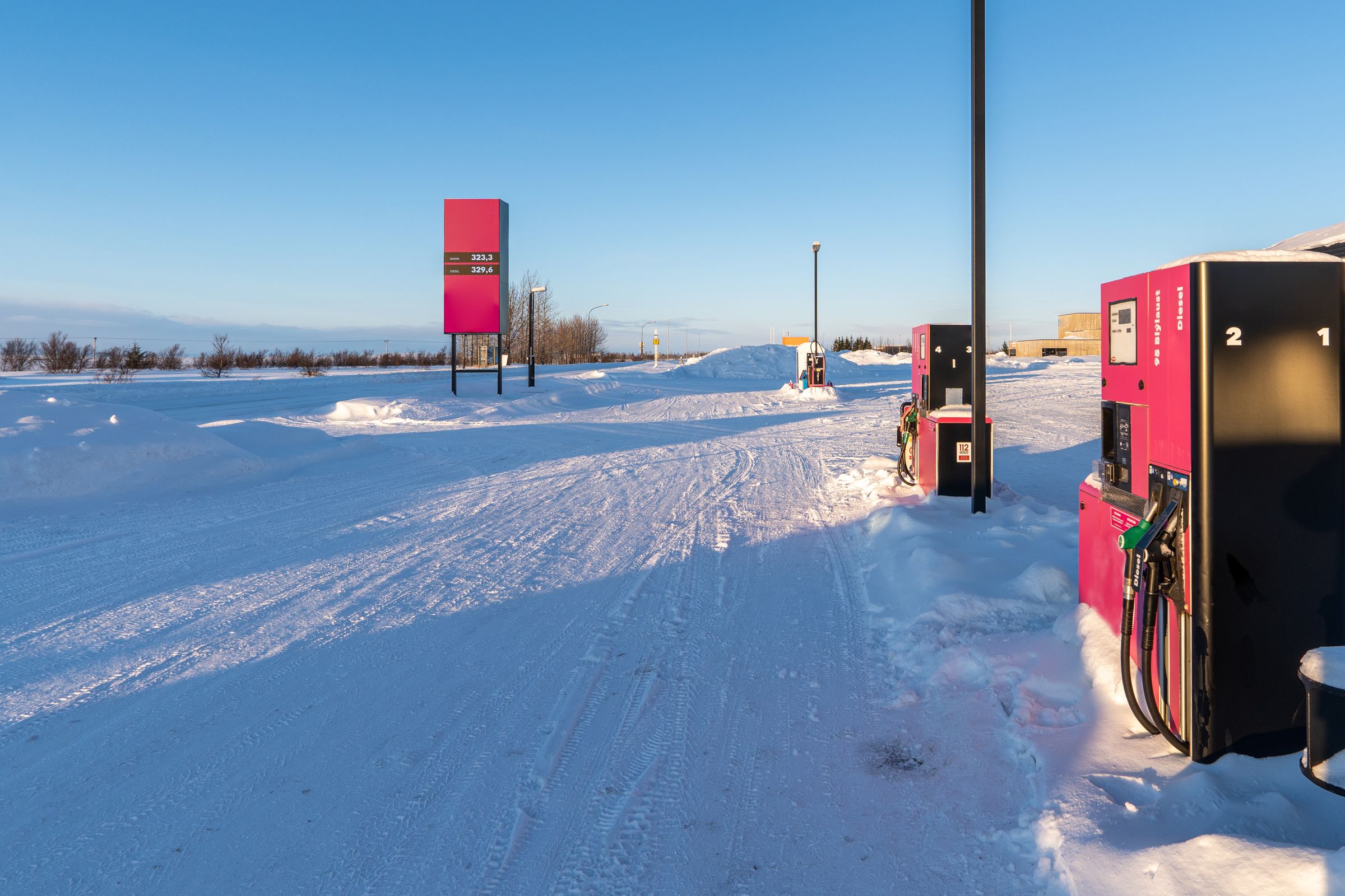 A gas station in a snowy landscape with pink pumps and a price sign under a clear blue sky.