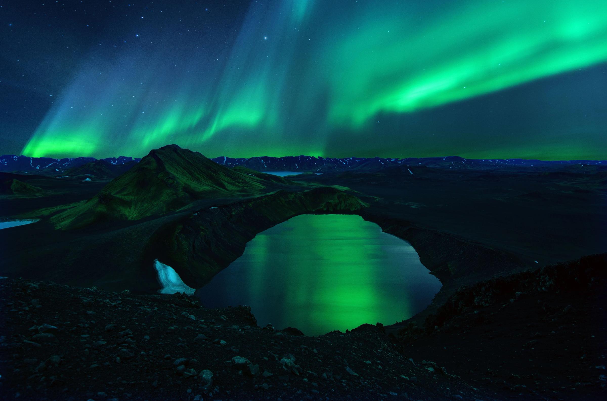 the aurora borealis is shining over a lake in the mountains .