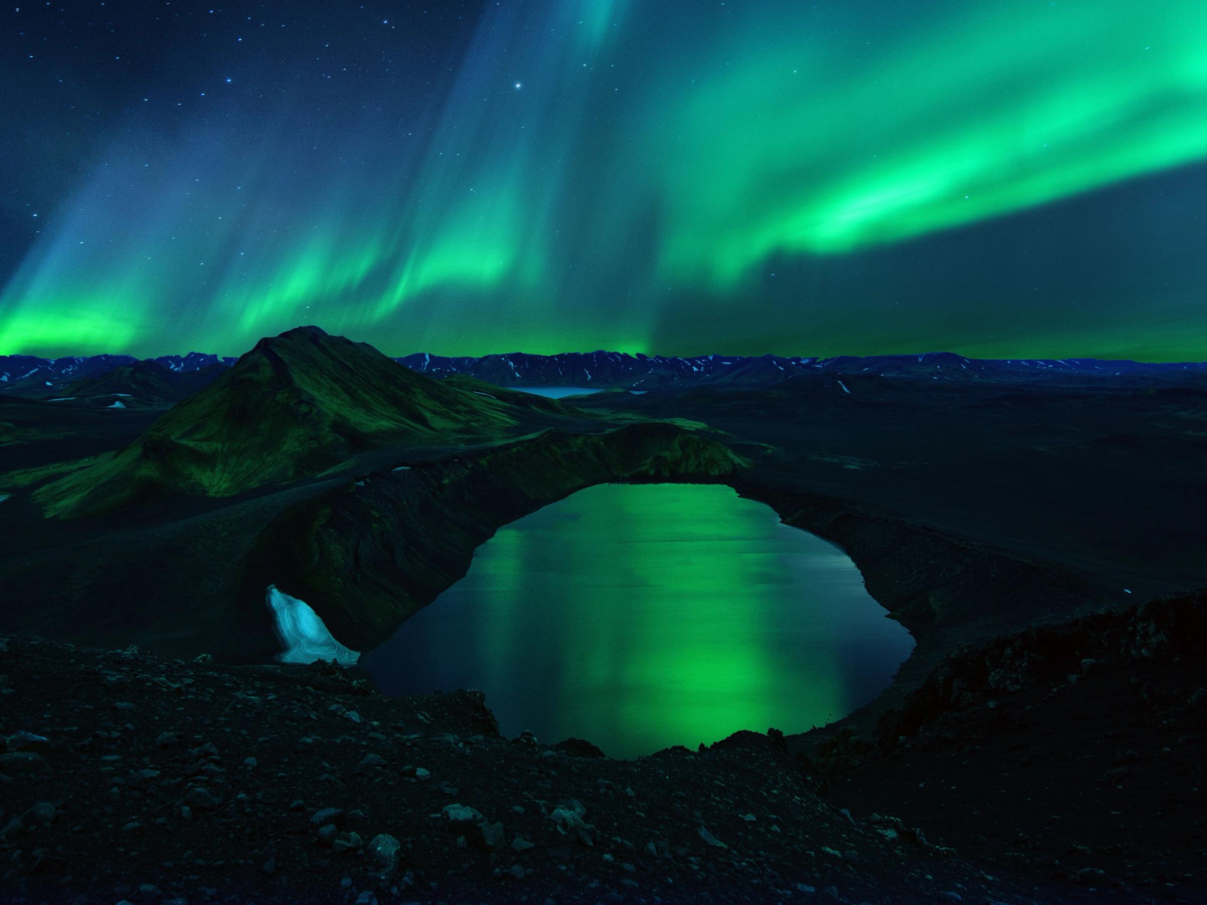 the aurora borealis is shining over a lake in the mountains .