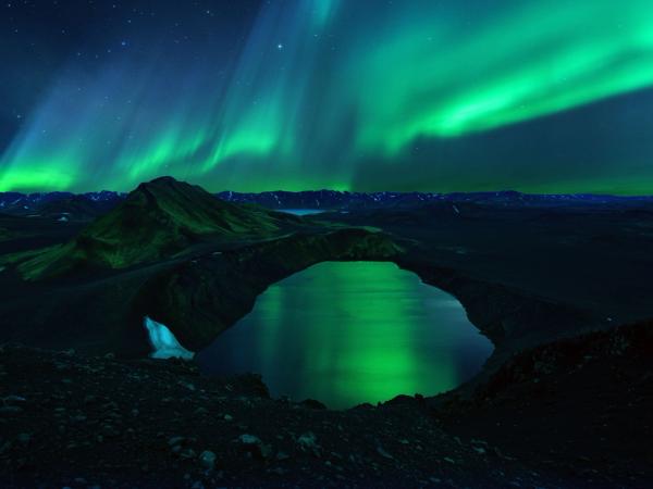 the aurora borealis is shining over a lake in the mountains .