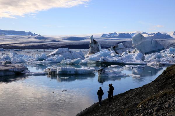 two people are standing on the shore of a lake surrounded by icebergs .