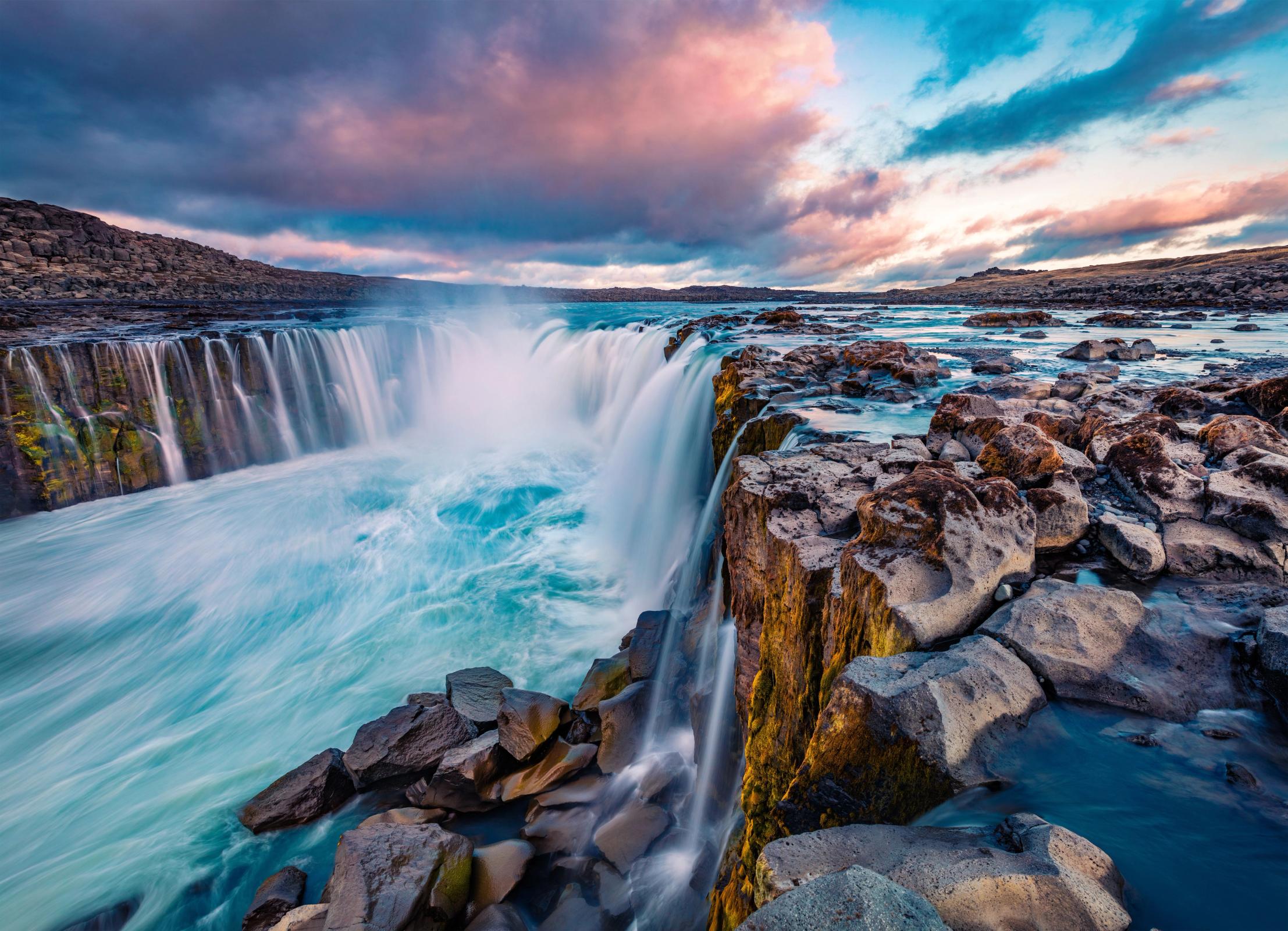 una cascada está rodeada de rocas en medio de un río .