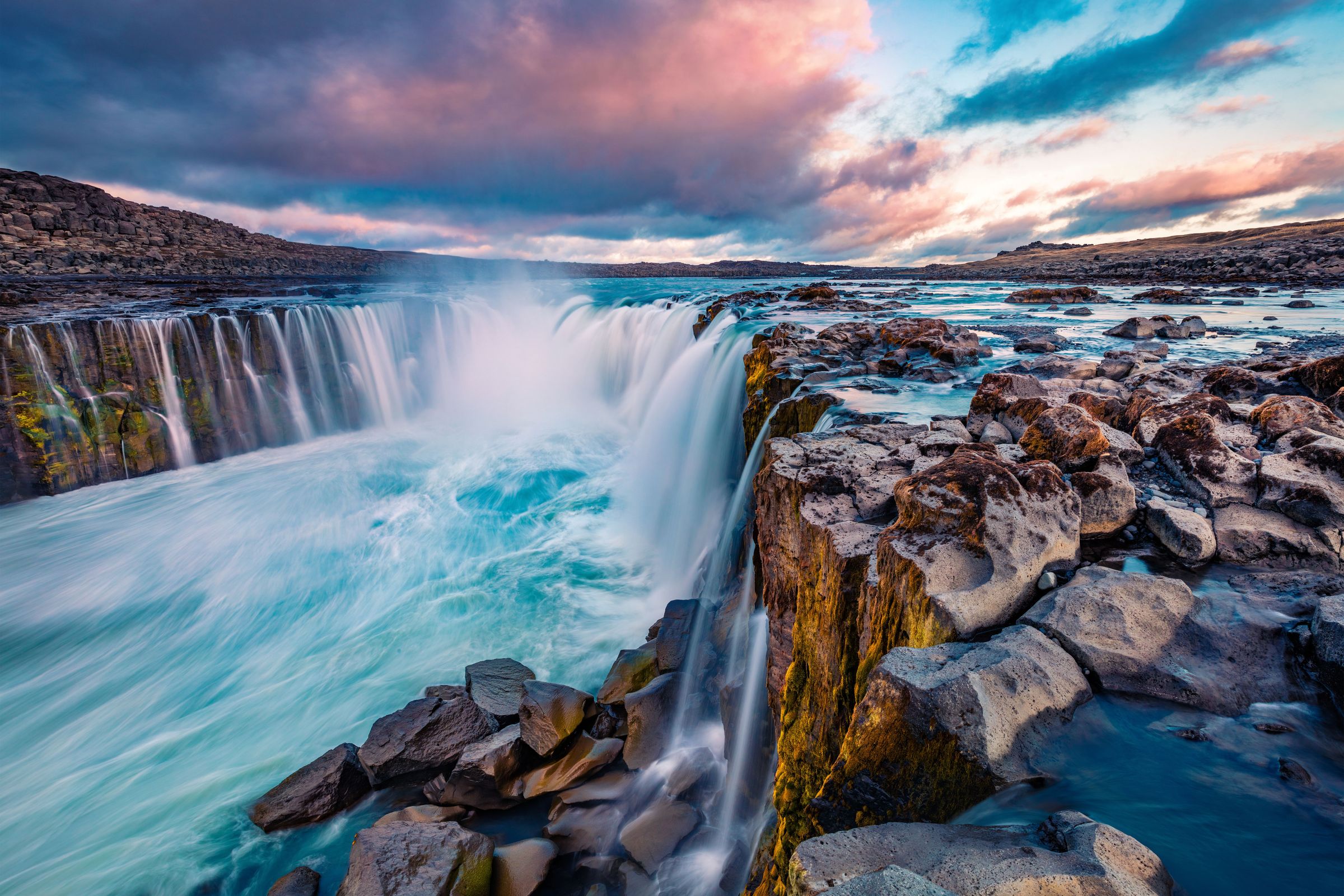 una cascada está rodeada de rocas en medio de un río .