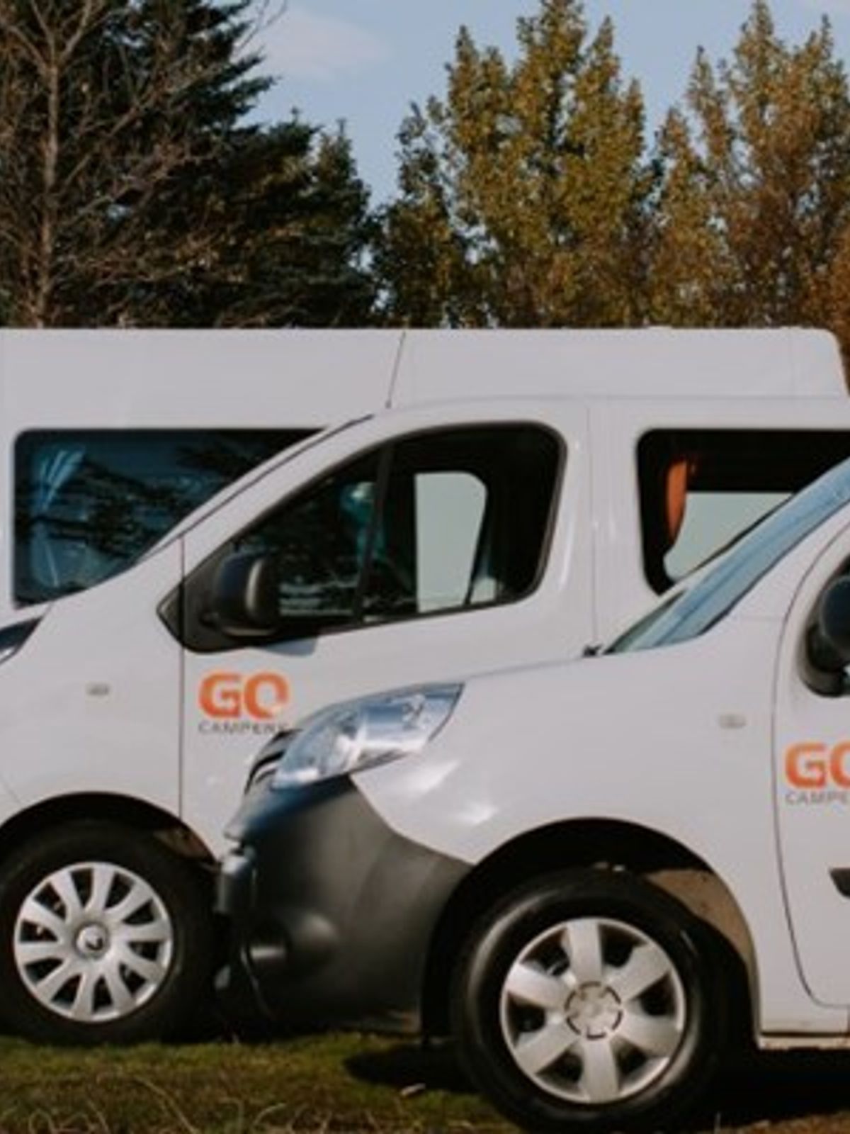 A row of white GO Campers vehicles, including vans and SUVs, parked outdoors.