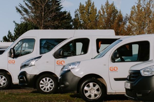 a row of white vans parked next to each other in a field .