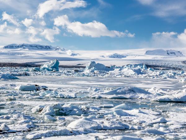 A glacial lagoon filled with icebergs with snow-covered mountains under a blue sky.