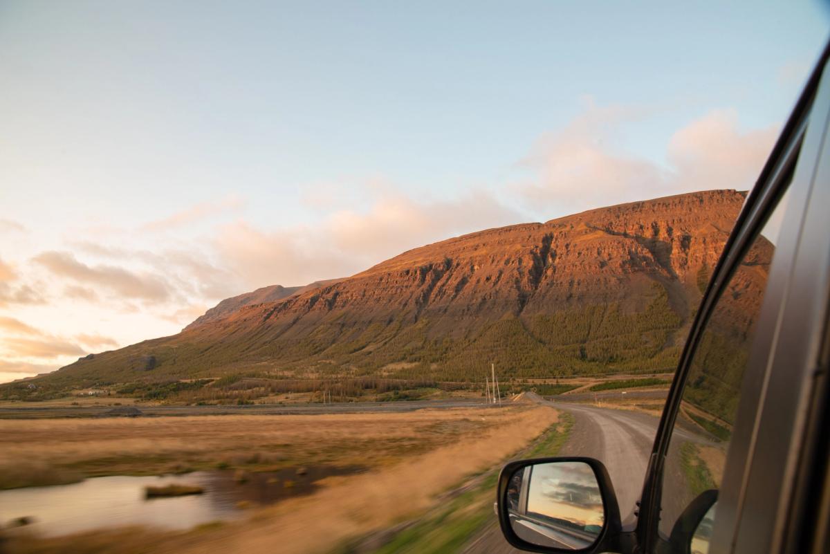 View from a Toyota Land Cruiser side window of a gravel road running below a mountain