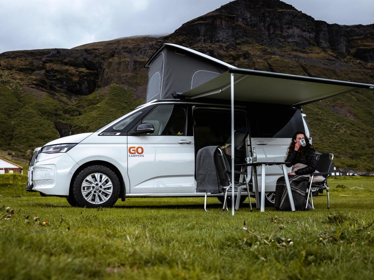 Hurð á 4x4 húsbíl opin Manneskja situr undir skyggni á fjórhjóladrifnum húsbíl með svefnplássi fyrir fjóra, húsbílaleiga á Íslandi