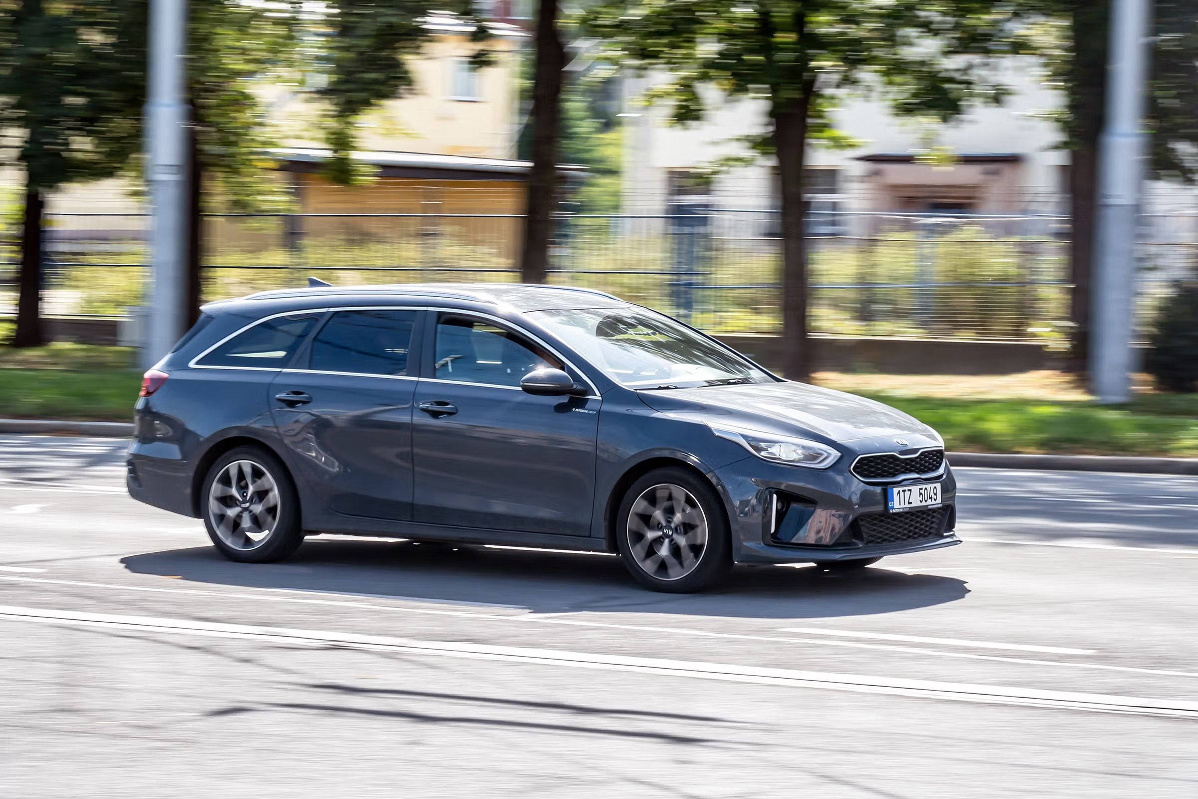 A dark grey station wagon drives on a street with a motion-blurred background.