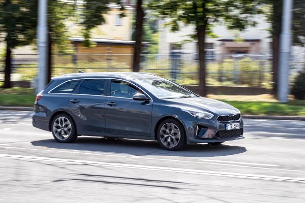 A dark gray station wagon drives on a street with a blurred background.