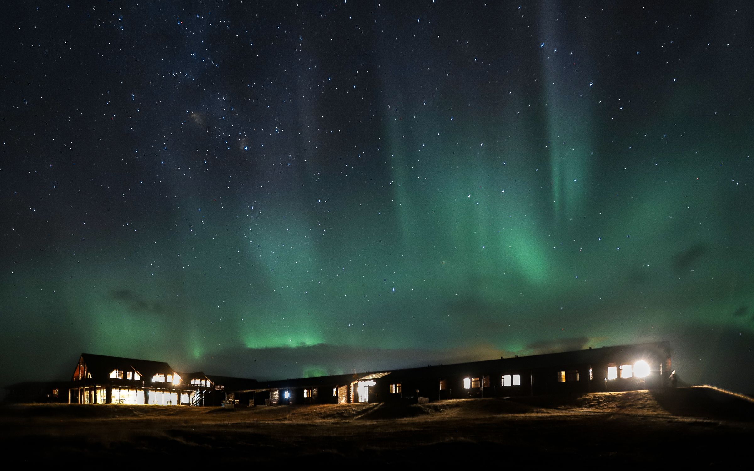 Una cabaña con ventanas iluminadas bajo un cielo estrellado y la aurora boreal verde.
