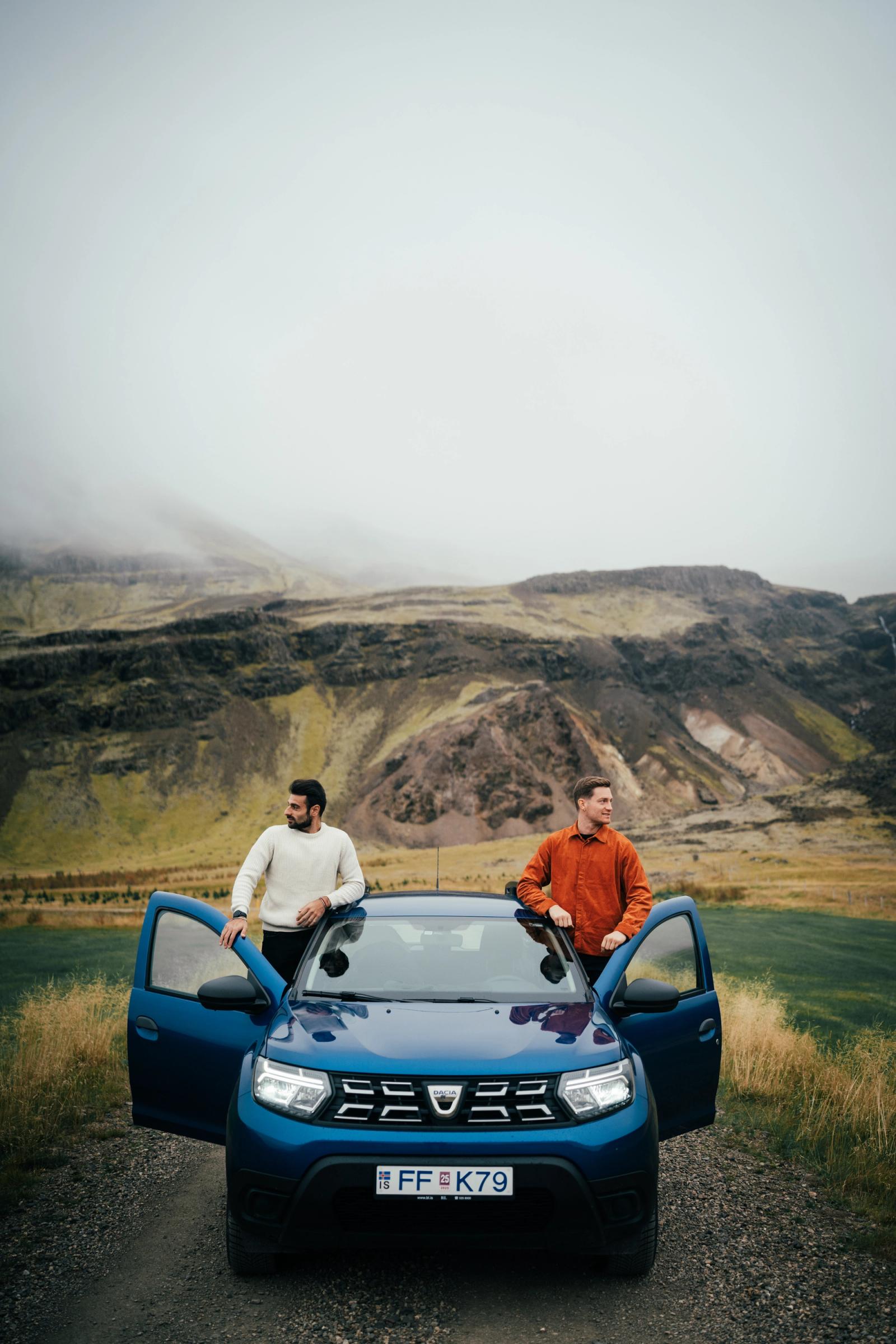 two men standing next to a blue dacia car