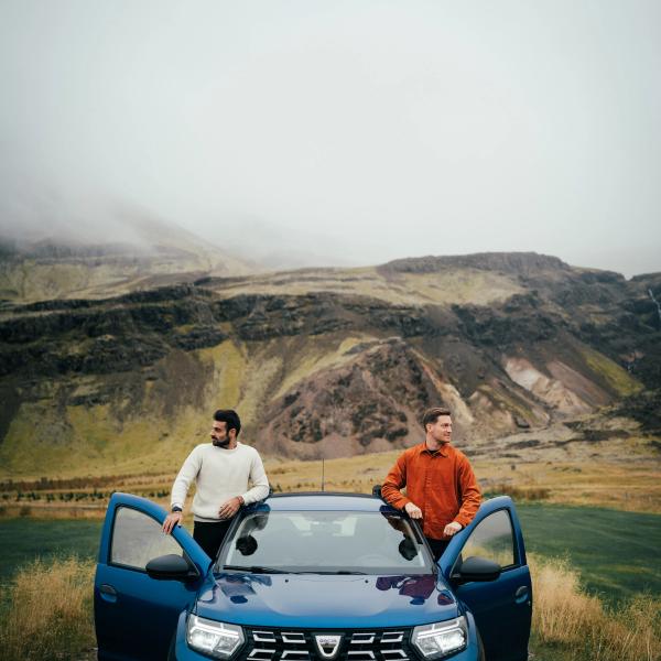 two men standing next to a blue dacia car