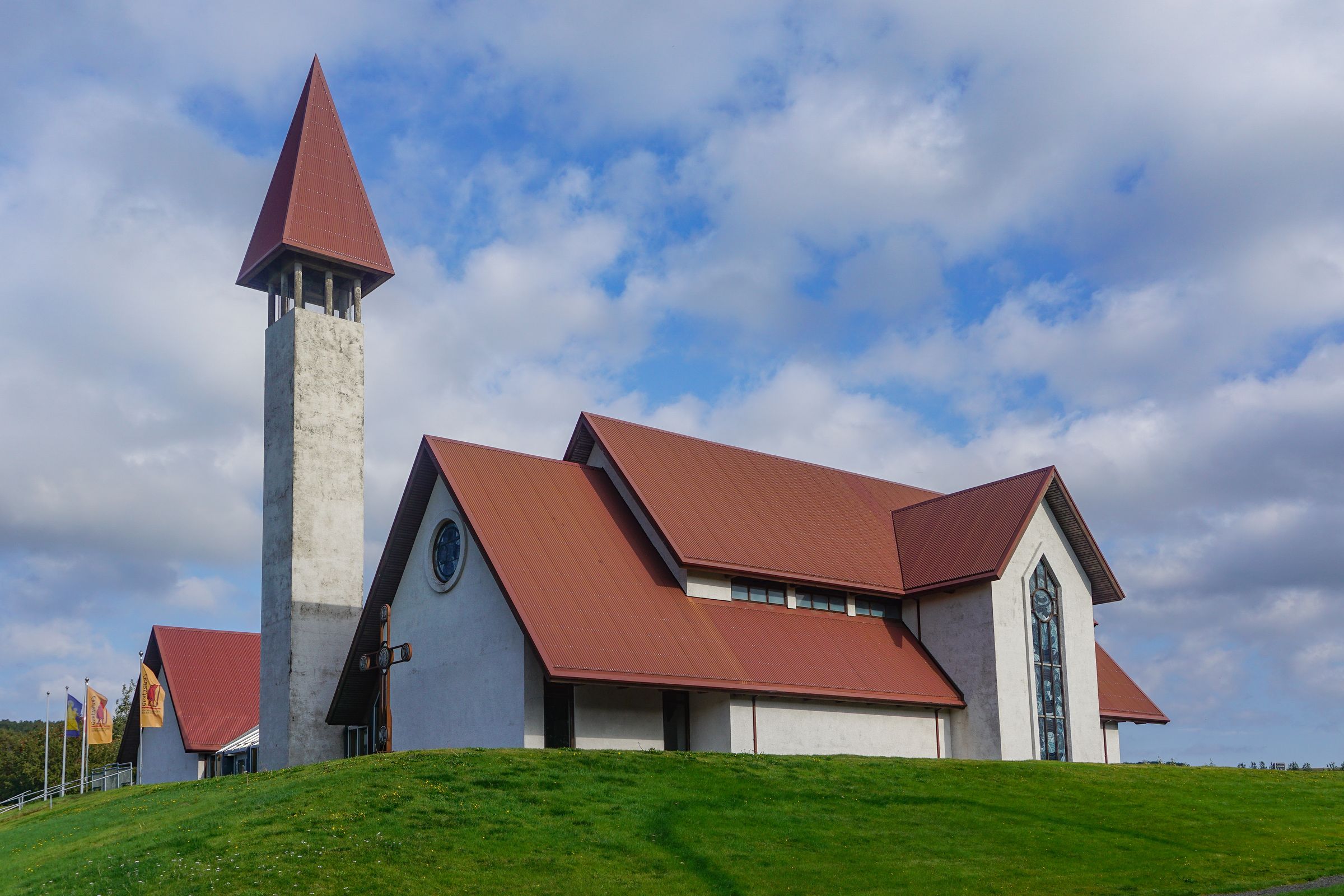 a church with a red roof is sitting on top of a grassy hill at Snorrastofa in Reykholt iceland.