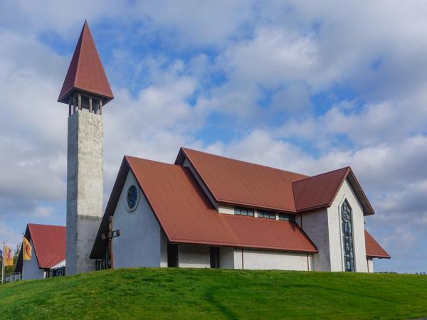a church with a red roof is sitting on top of a grassy hill at Snorrastofa in Reykholt iceland.