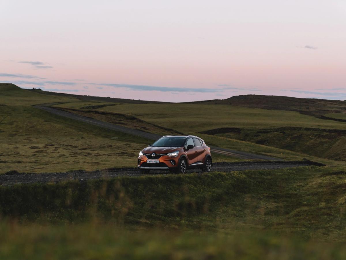 Vista panorámica abierta del Renault Captur Renault Captur de viaje por carretera en Islandia, aparcado en un camino de grava entre verdes colinas